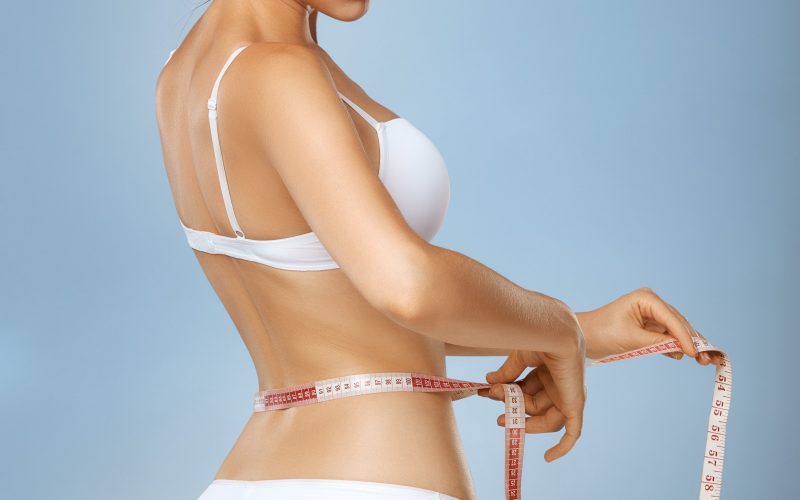 Slender woman measuring her waist with metric tape measure after a